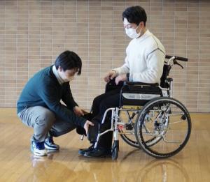 車椅子の操作を説明する学生
