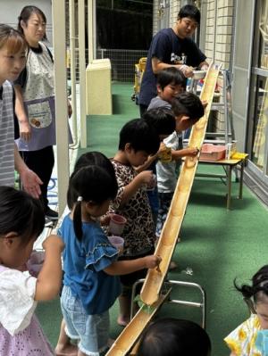 男性保育士が流しているそうめんを食べている子ども達