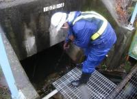 金属の網のパネルに立ち、水路清掃をしている男性の写真