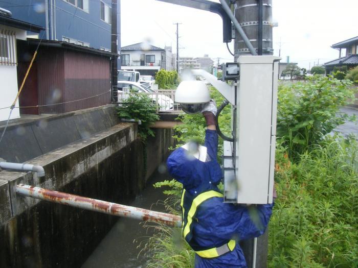 雨具を着用した男性が、高所のウェブカメラを清掃している様子